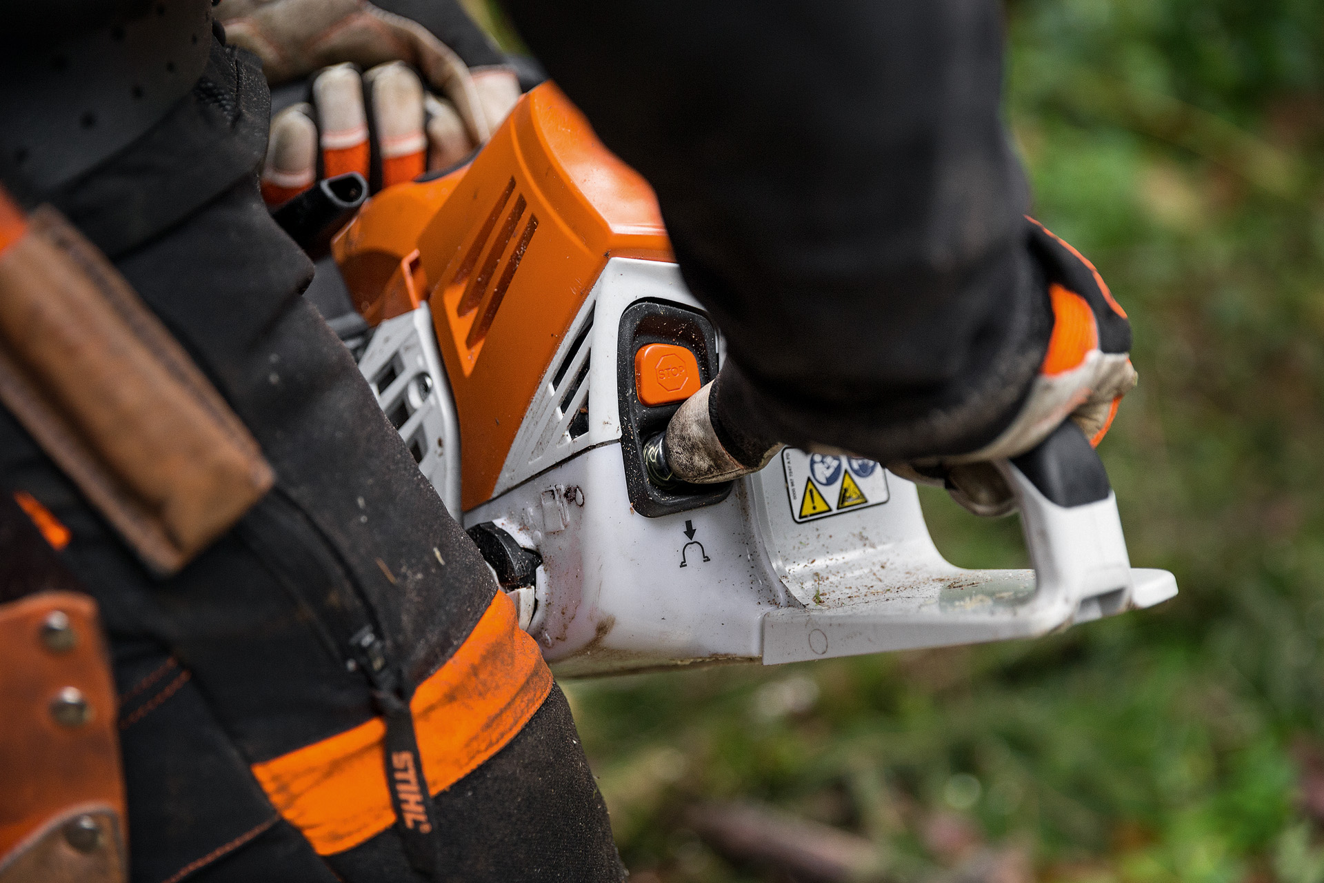 O persoană în îmbrăcăminte de protecție pornește motoferăstrăul pe benzină STIHL MS 500i la sol într-o pădure de foioase