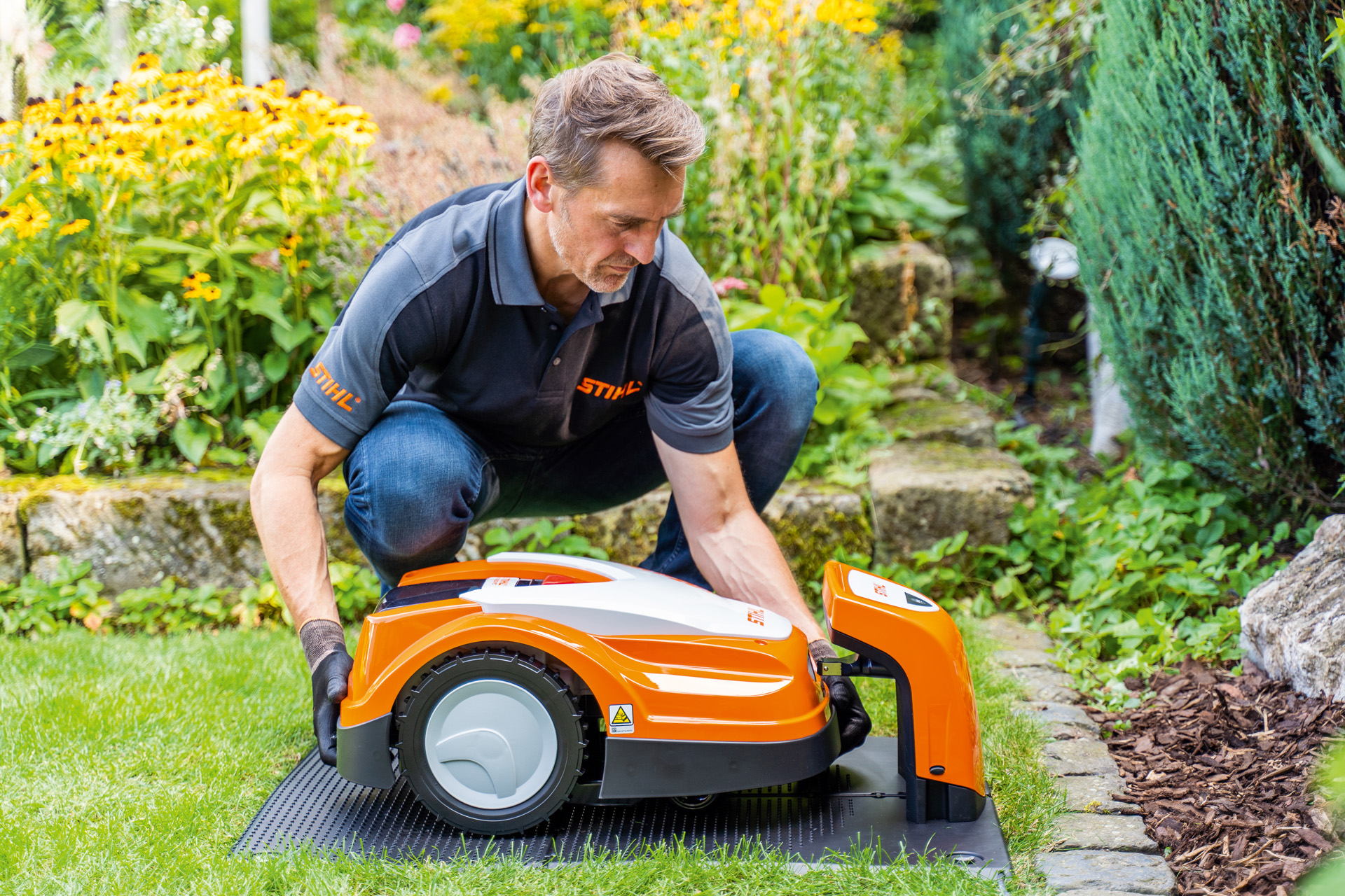 Un distribuitor STIHL plasează un robot de tuns iarba STIHL iMOW în stația sa de încărcare într-o grădină